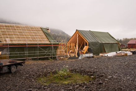 Vedvarende regn i Kongsbergtraktene krevde full tildekning av de halvferdige halmhusene som etterhvert får sibirsk lerk som taktekking og leirpuss på veggene både ute og inne. Byggverket er tegnet av arkitektene Rolf Jacobsen og Arild Berg.