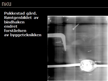 Klikk for stort bilde. Røntgenbilde av et utsnitt av laftet og tosidig panelt yttervegg på Pukkestad gård, Sandefjord. Bindhaken (den grå kroken til venstre) som ble oppdaget ved hjelp av røntgenundesøkelsen, vakte stor forbauselse. Ytterligere undersøkelser viste at bindhaken ligger nedfelt i laftestokken, slik at den kun ville blitt oppdaget dersom bygningen ble revet. Samtlige stokker på denne ytterveggen var, på grunn av veggens lengde, skjøtet ved hjelp av bindhaker. Dette er en svært uvanlig bygningsteknikk. (Foto: NIKU)